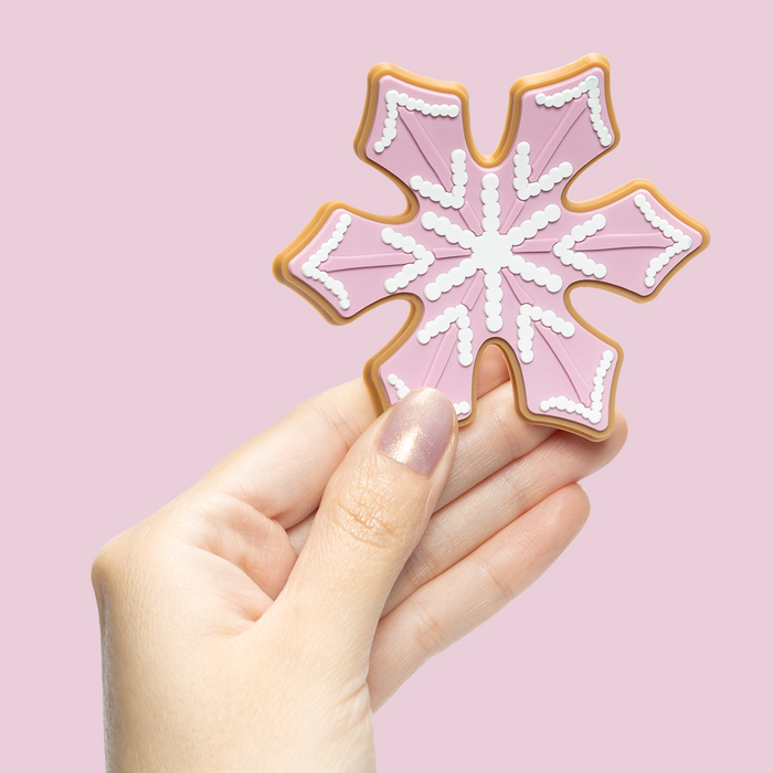 Hand with short nails painted in Star Baker sheer iridescent lavender gel polish holding pink snowflake cookie on light pink background