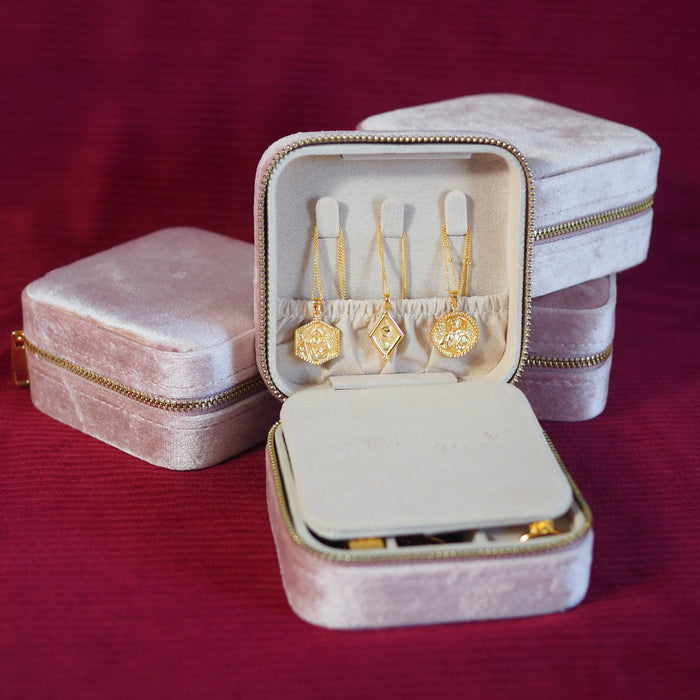 Blush pink travel jewellery case with gold jewellery necklaces inside on a red background