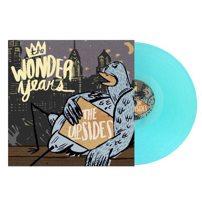 A light blue vinyl record by The Wonder Years slides from its cover, which shows illustrated city buildings at night, a pigeon with a box labeled The Upsides, and bold lettering referencing Logan Circle.