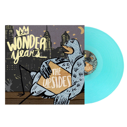 A light blue vinyl record by The Wonder Years slides from its cover, which shows illustrated city buildings at night, a pigeon with a box labeled The Upsides, and bold lettering referencing Logan Circle.