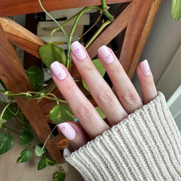 Tiny Heart Tattoo - Press-On | Short | Squoval showing hand with pale pink short squoval press-on nails featuring small outlined heart design