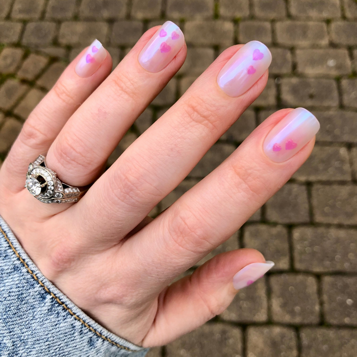 Tiny Puffy Hearts - Press-On | Short | Squoval showing hand with short squoval nails featuring iridescent base and small pink puffy hearts
