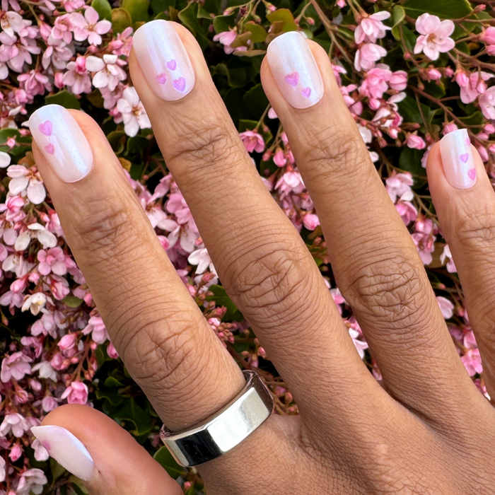 Tiny Puffy Hearts - Press-On | Short | Squoval showing hand with short squoval nails featuring iridescent base and delicate pink heart accents