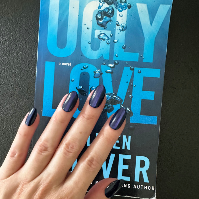 Velvet Rain - Press-On | Medium | Oval showing dark blue shiny velvet-effect medium oval press-on false nails on hand over book cover