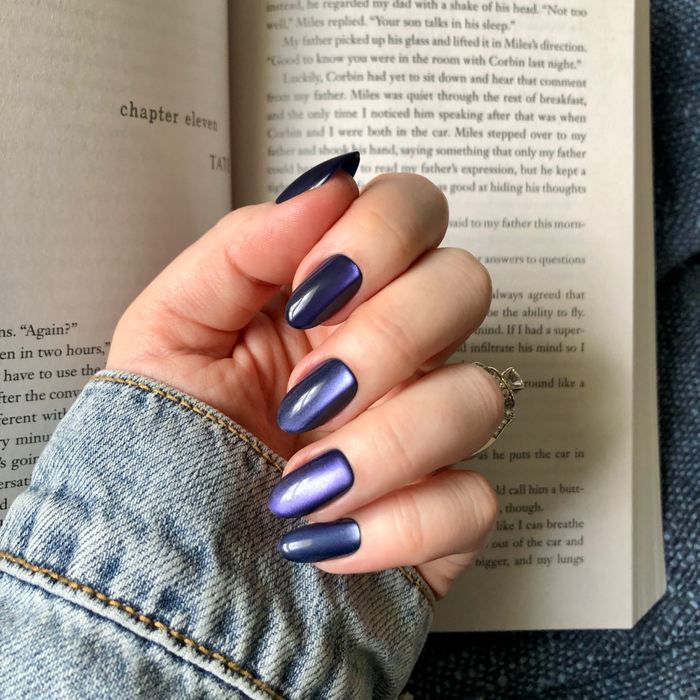 Velvet Rain - Press-On | Medium | Oval showing medium oval press-on false nails in shiny dark blue velvet mani on hand over book pages